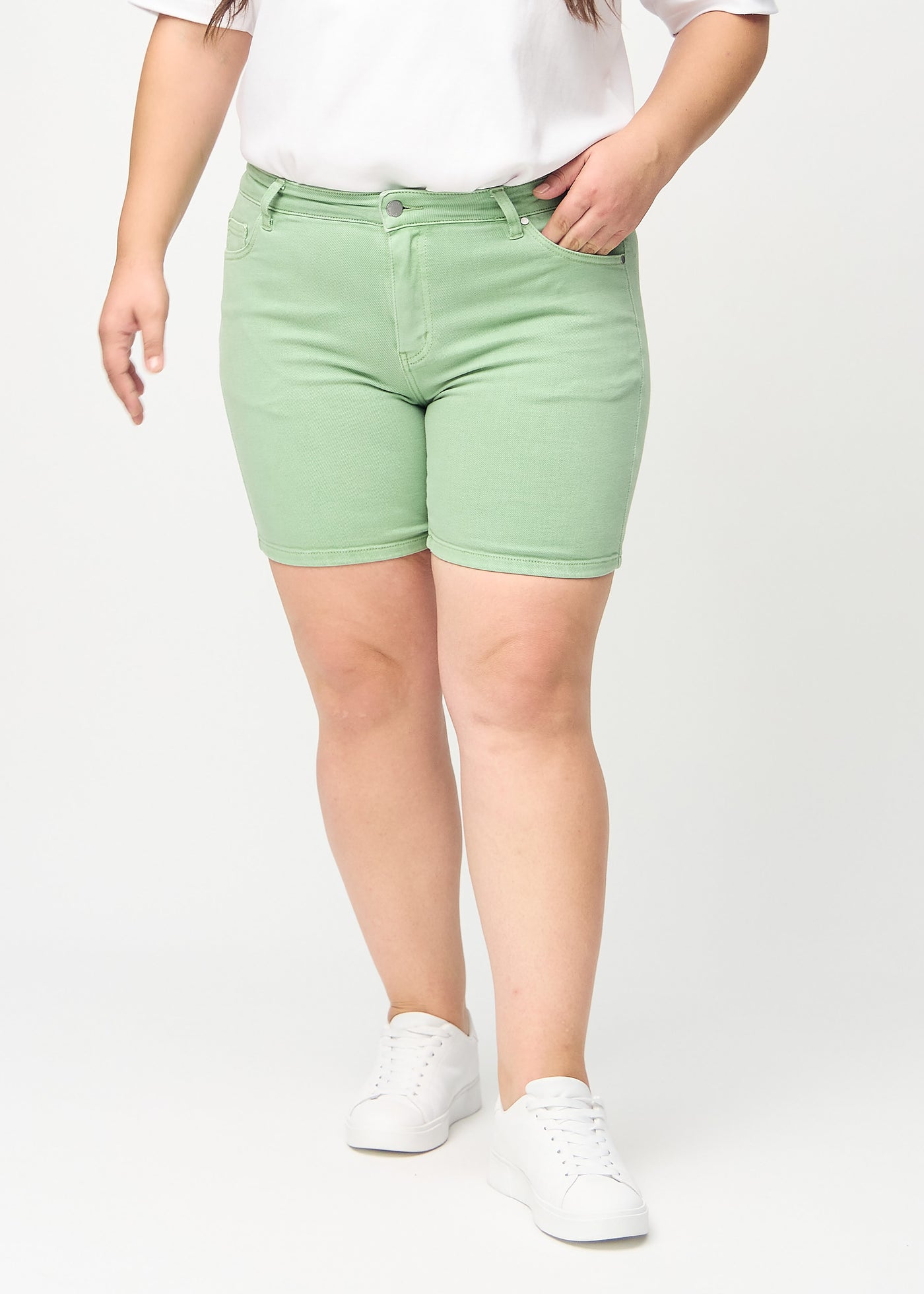 Lysegrønne skinny short shorts, modelnavn Mints, som sidder tæt til, og slutter midt på låret på en plus-size model, set forfra.